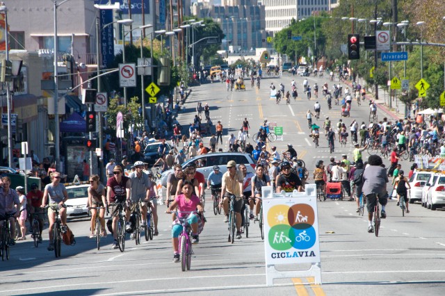 Dozens of cyclists on a six-lane city street, closed to cars, with the sign "CicLAvia" in front.